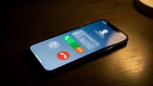 Smartphone posé sur un bureau sombre, affichant une notification abstraite d’appel manqué dans une ambiance domestique sobre associée à la cybersécurité.