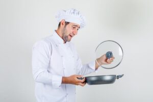Cuisinier comparant plusieurs poêles sur un plan de travail en cuisine.