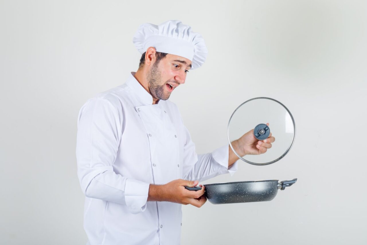 Cuisinier comparant plusieurs poêles sur un plan de travail en cuisine.
